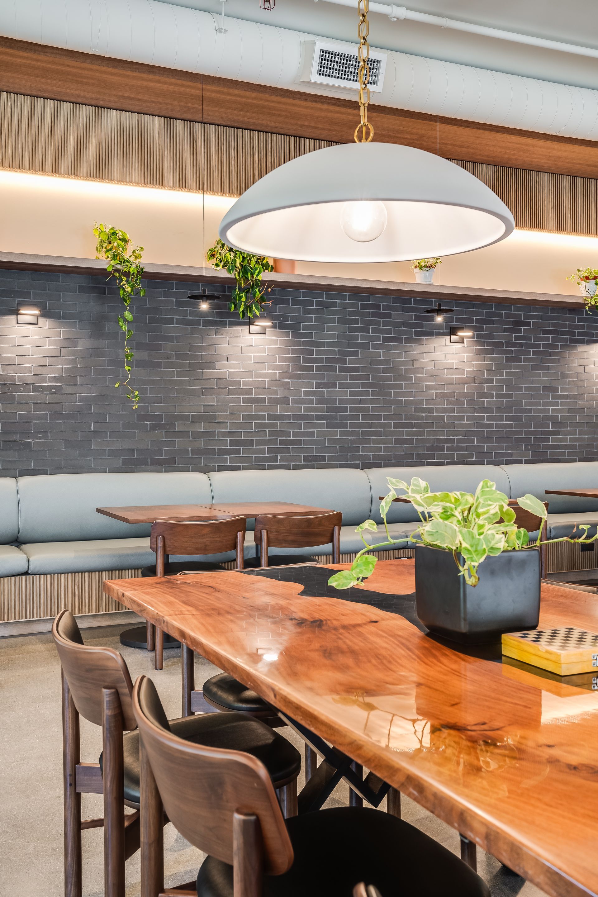 Modern café interior with wooden tables, hanging pendant light, and dark brick wall with plants