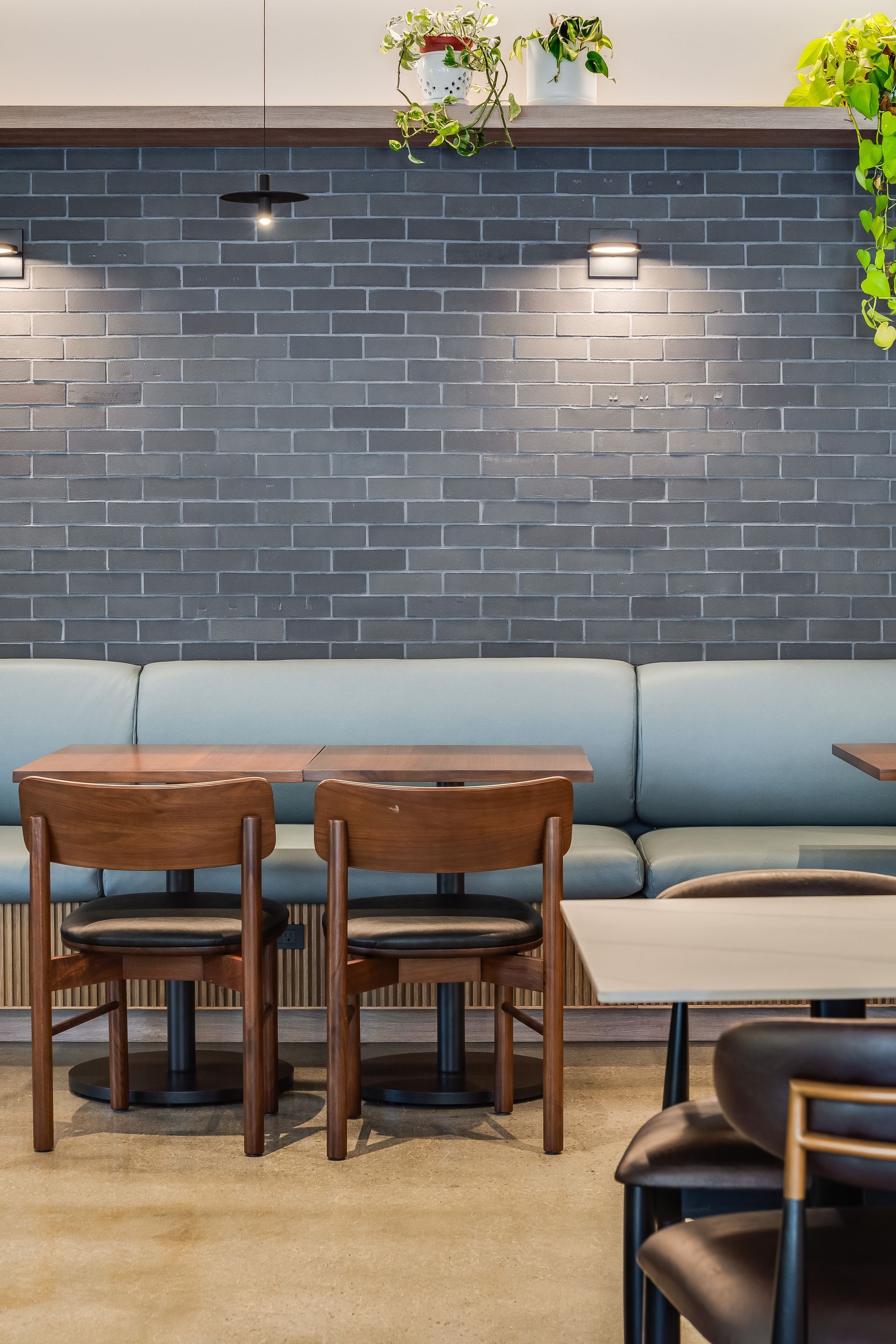 Modern cafe interior with blue banquette seating, wooden tables, and a dark brick wall with lights