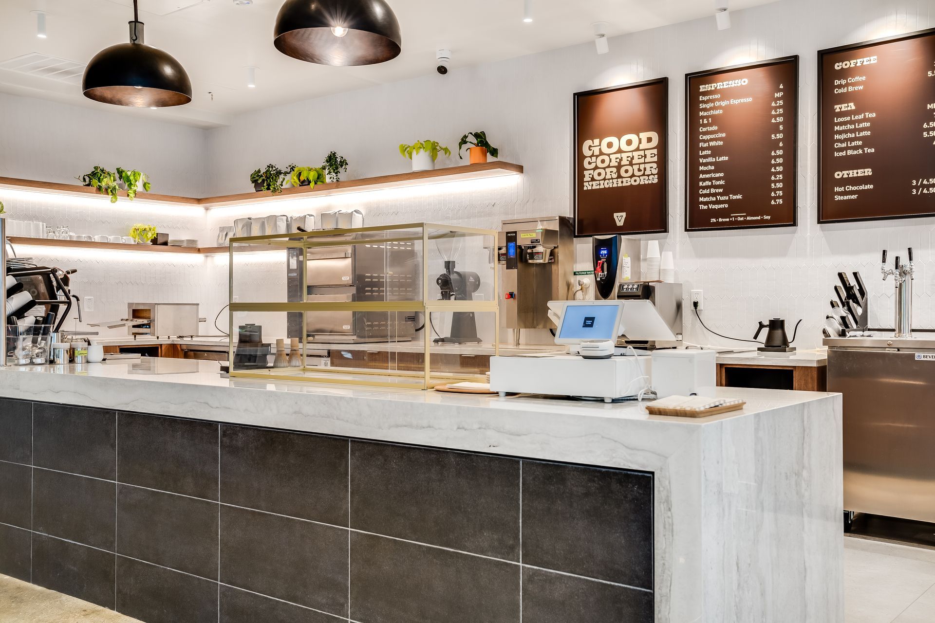 Bright modern café interior with white counter, menu boards, pastries, and pendant lights
