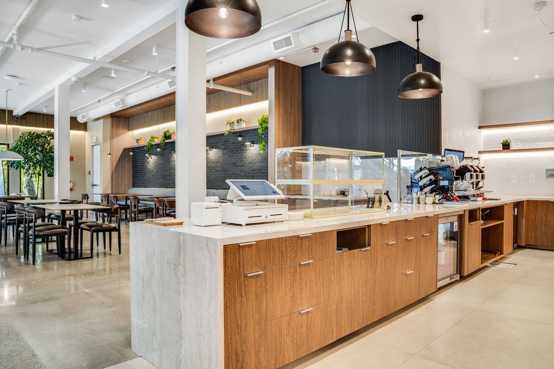 Modern café counter with wood cabinets, white stone top, pendant lights, and seating in a bright open interior