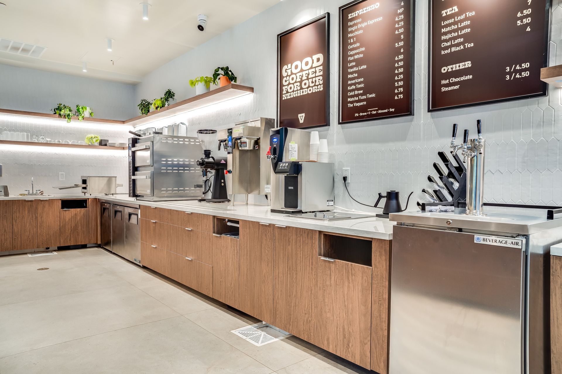 Modern cafe counter with wooden cabinetry, menu boards, espresso machines, and bright white walls