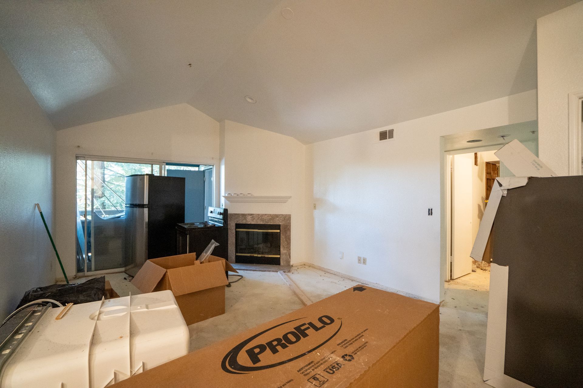 Cluttered living room with moving boxes, fireplace, and a large TV near an open doorway