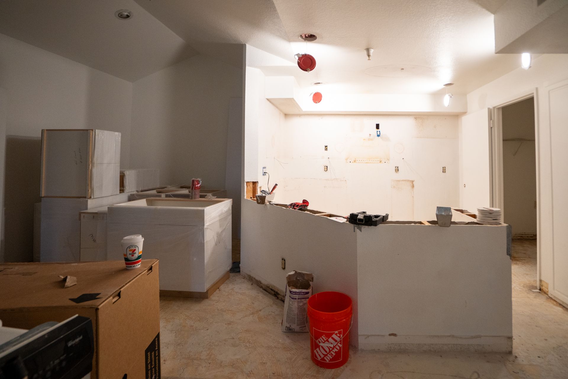 Partially renovated kitchen with white cabinets, refrigerator, countertop, and red bucket on the floor