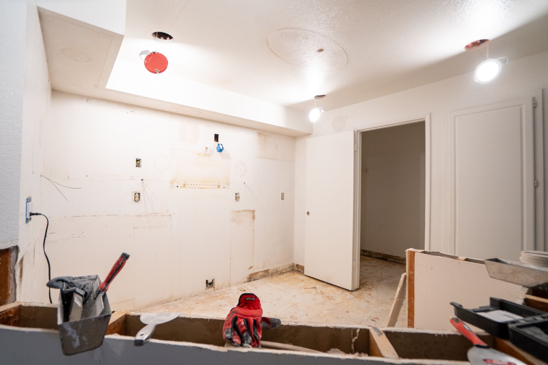 Empty white room under renovation, with tools, unfinished walls, and exposed flooring.