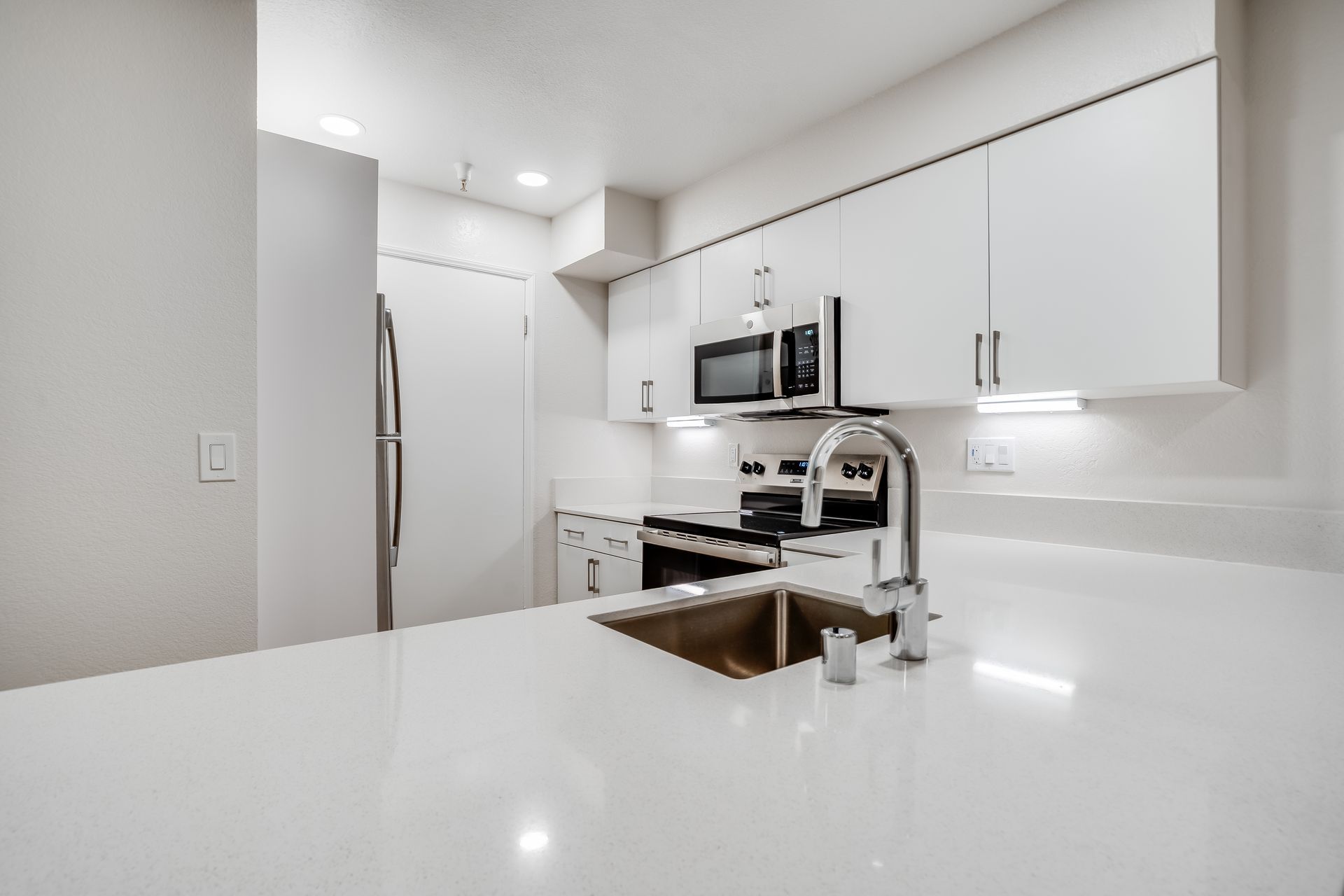 Bright modern white kitchen with island sink, stainless appliances, and minimalist cabinets