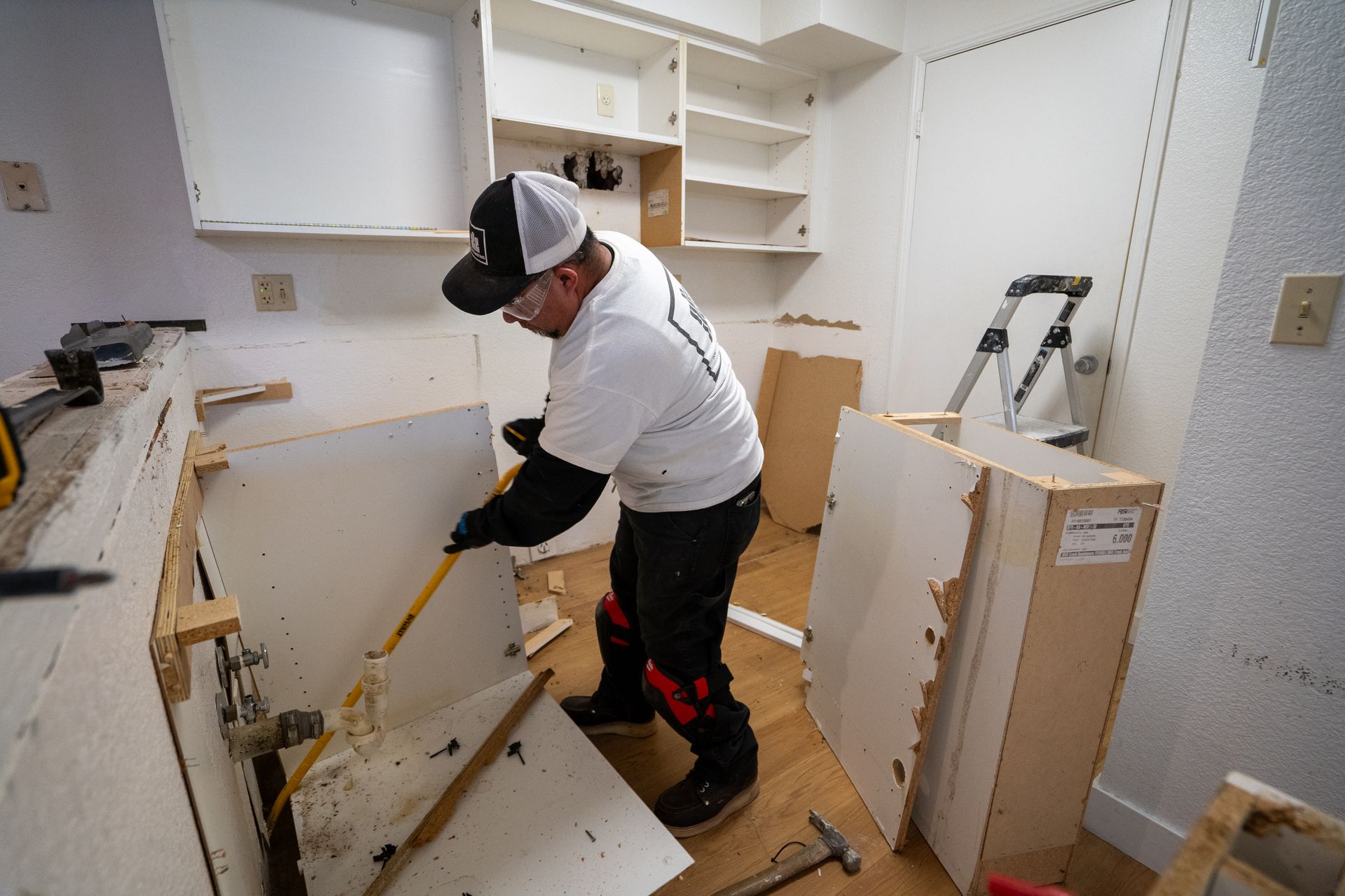Worker in a kitchen, prying up flooring with a crowbar during renovation.