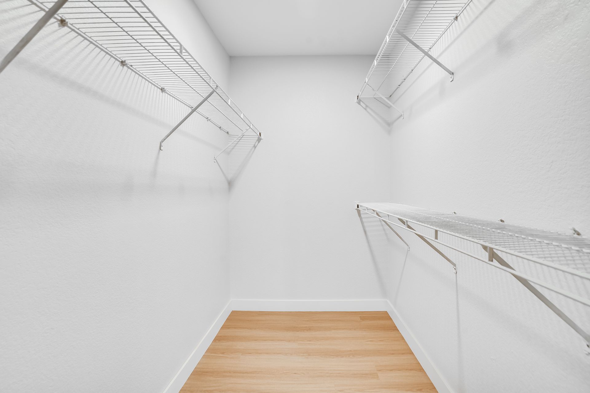Empty white walk-in closet with wire shelving and a light wood floor