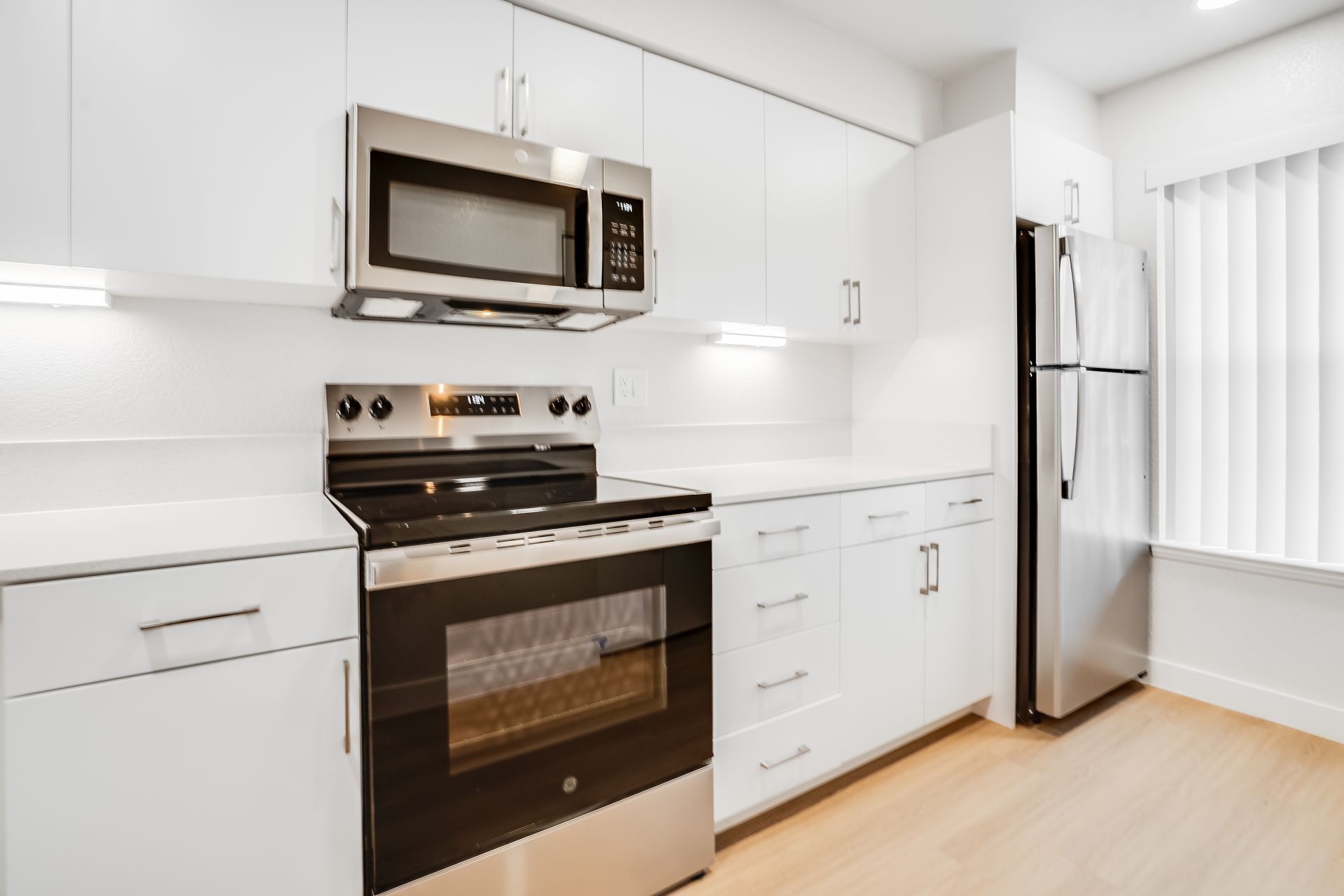 Bright modern kitchen with white cabinets, stainless steel appliances, and light wood flooring.