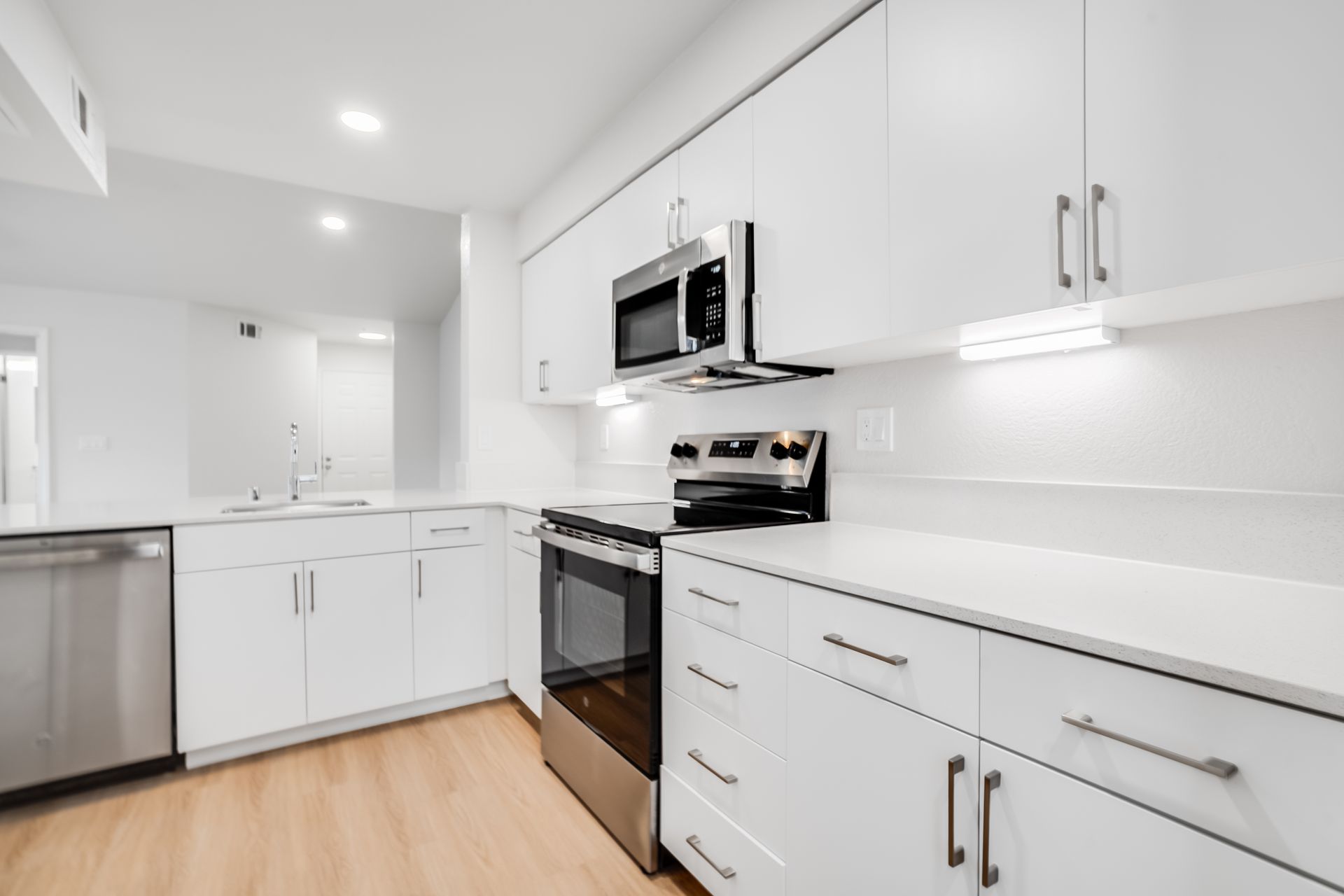 Bright modern white kitchen with stainless steel appliances, cabinets, and light wood flooring