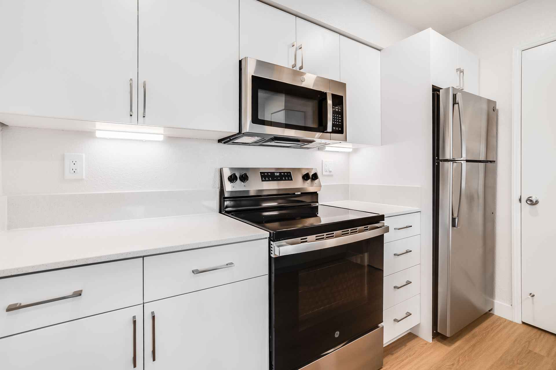 Modern white kitchen with stainless steel appliances, black stove, and hardwood floor