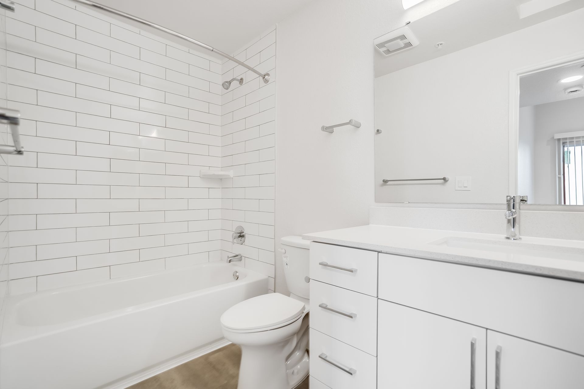 Bright white bathroom with bathtub, toilet, vanity, and large mirror.