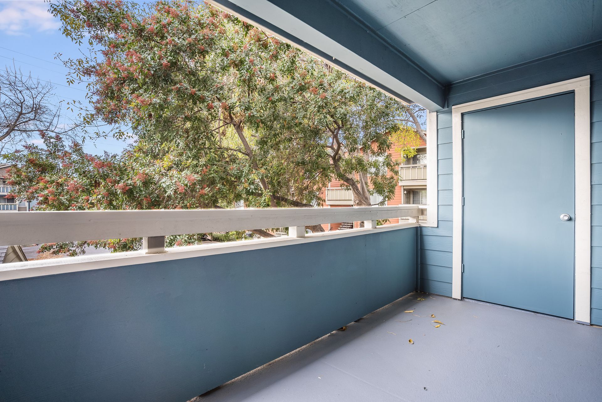 Small balcony with blue walls and door, overlooking trees and nearby buildings