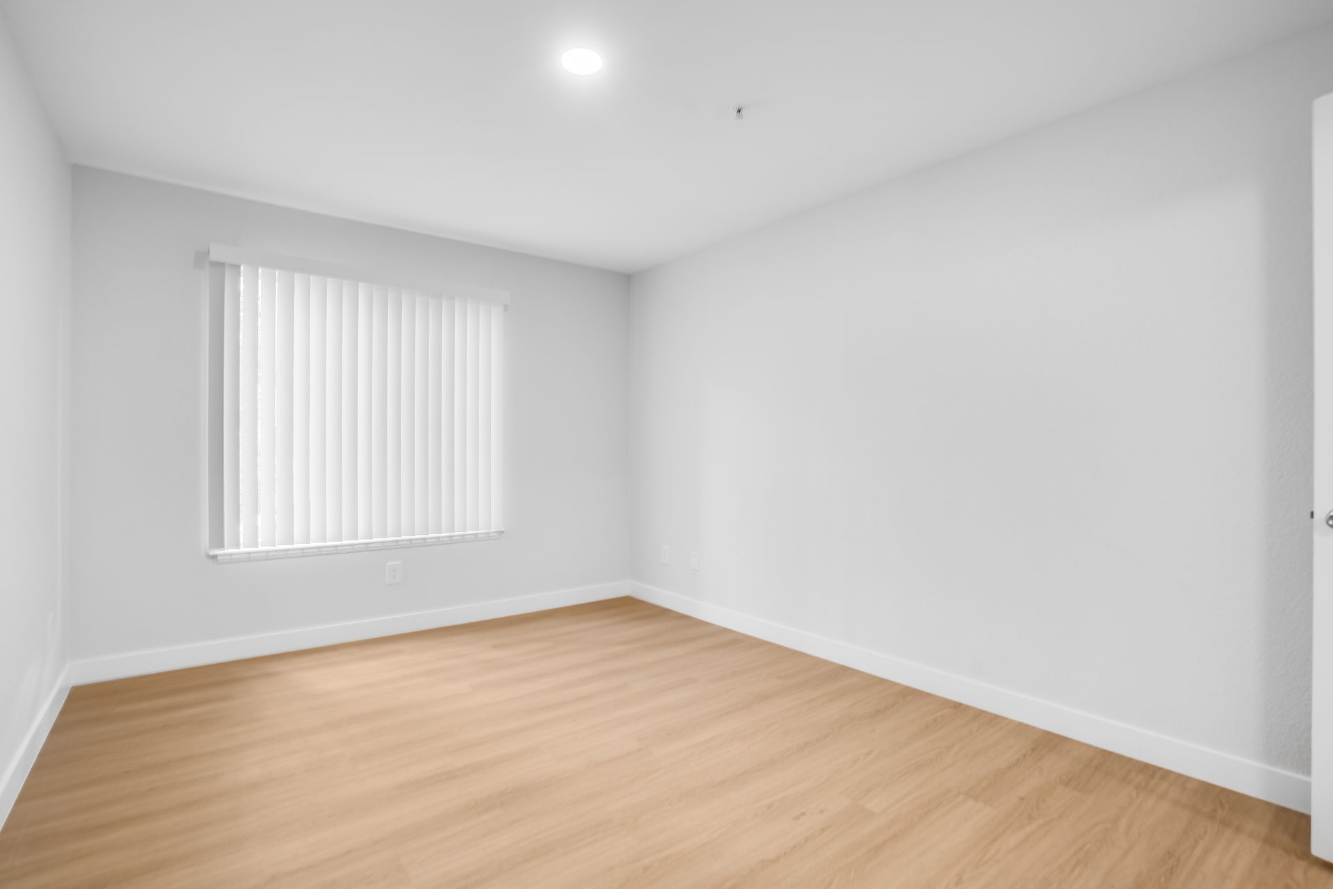 Empty white room with light wood floor and a window with vertical blinds