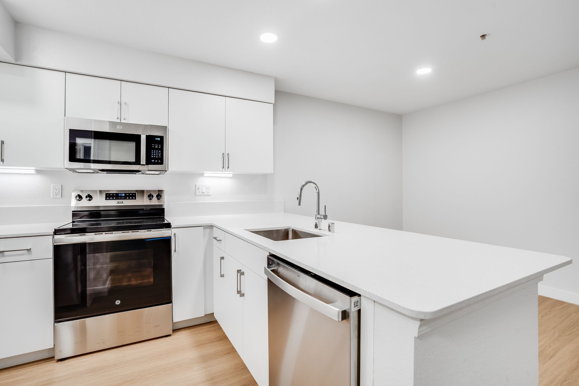 Bright modern white kitchen with stainless steel appliances, island sink, and light wood floor