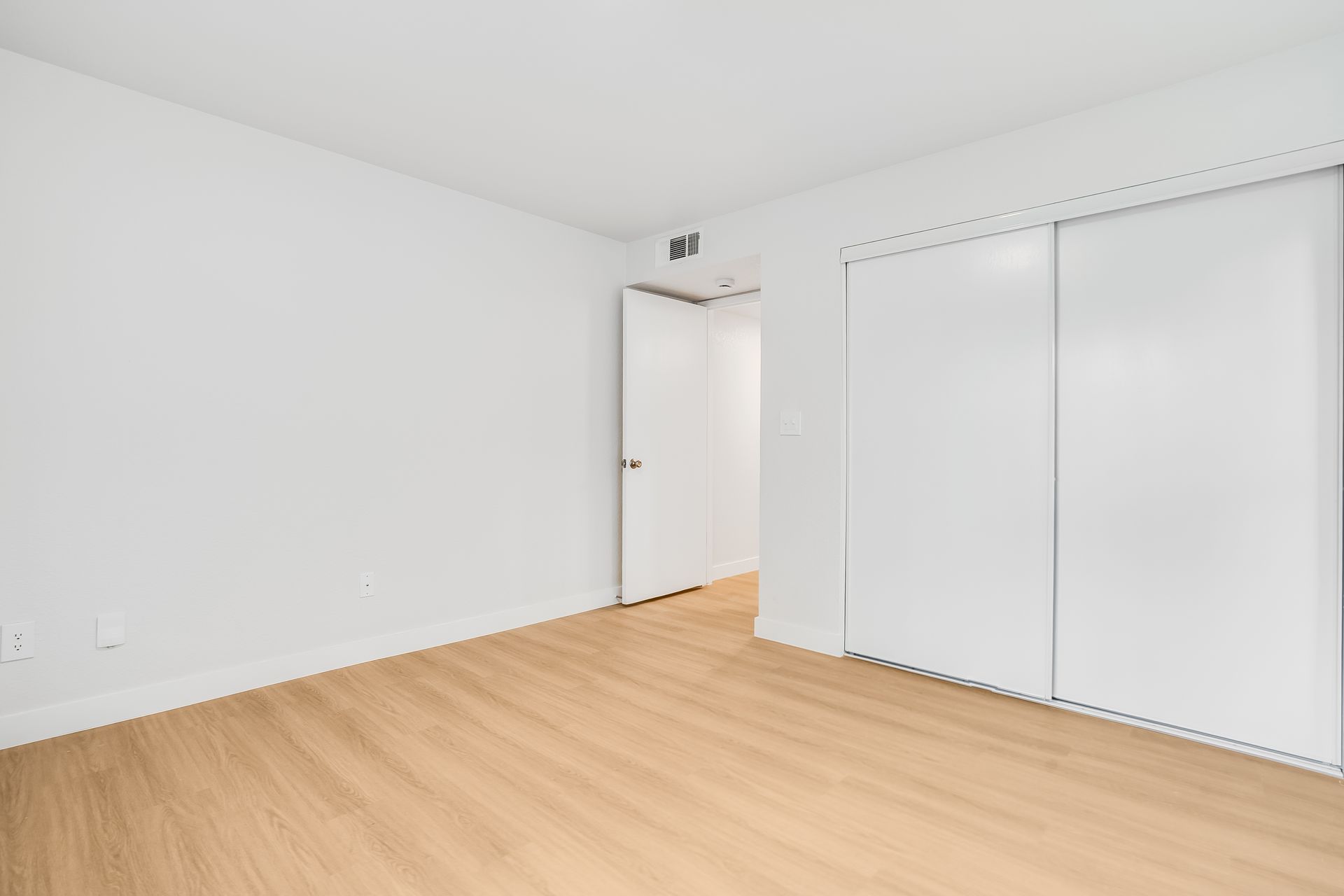 Empty white room with light wood floor, closet doors, and an open doorway