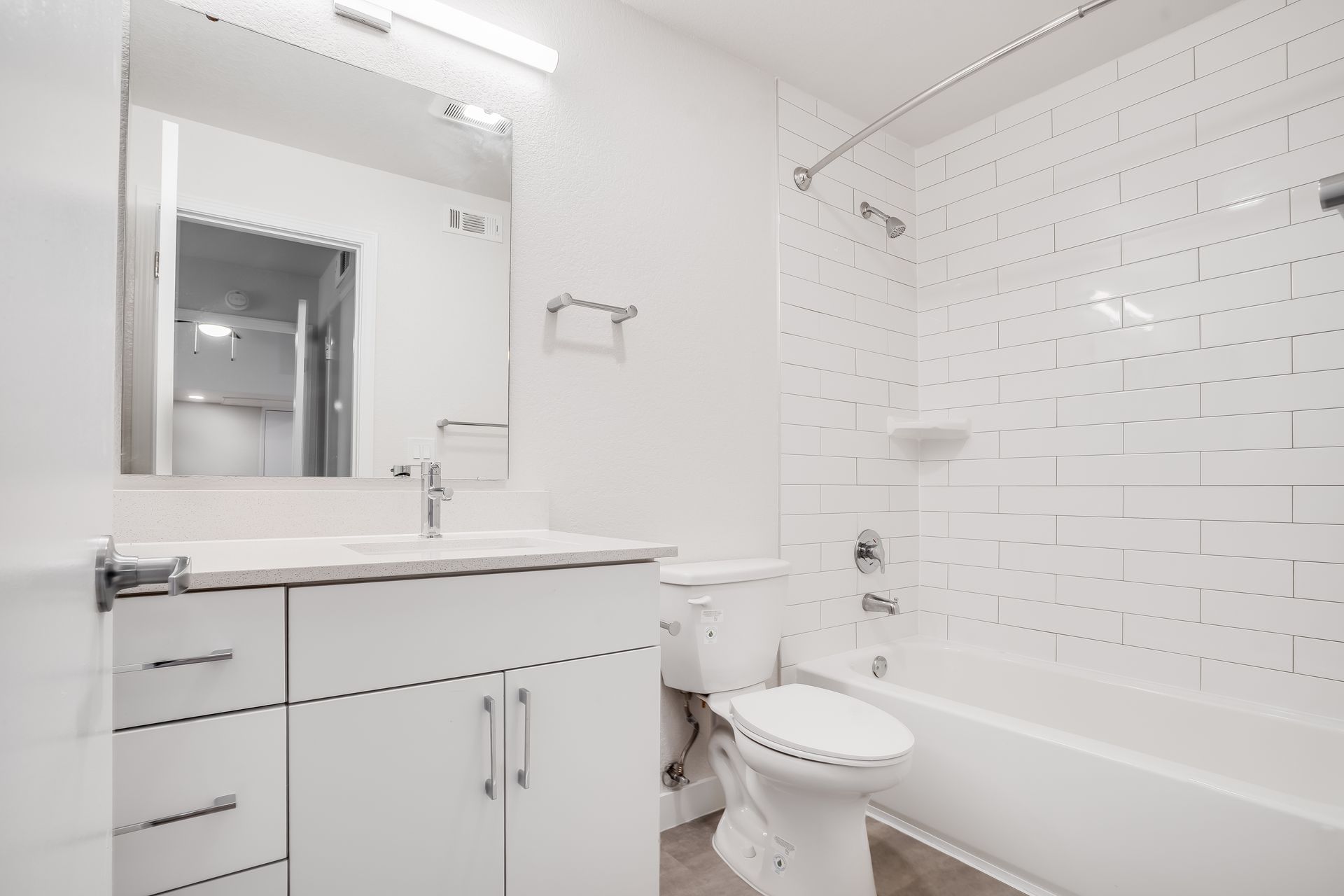 Bright white bathroom with vanity, mirror, toilet, and shower-tub with subway tile walls.