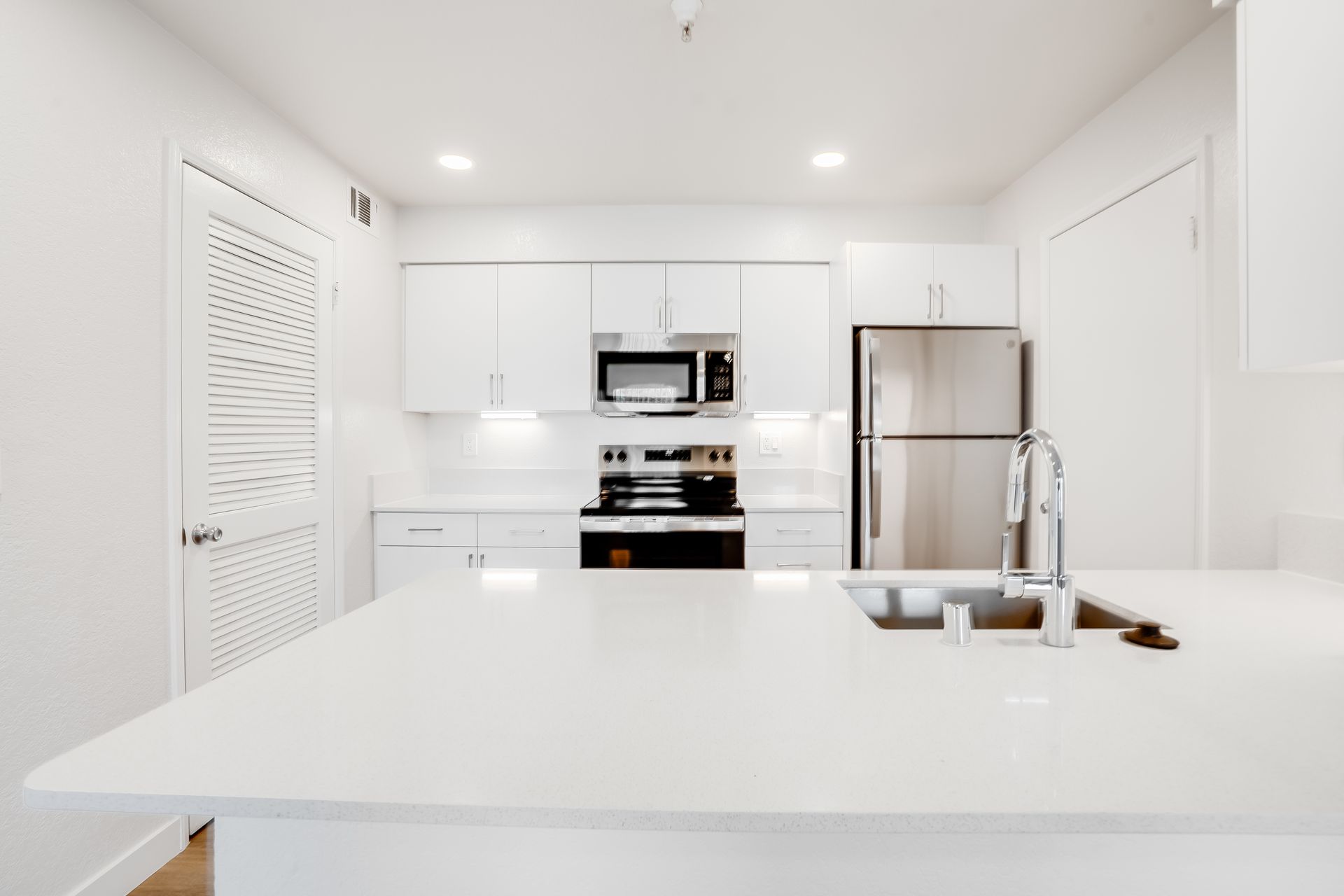 Bright white modern kitchen with island, stainless steel appliances, and sink faucet