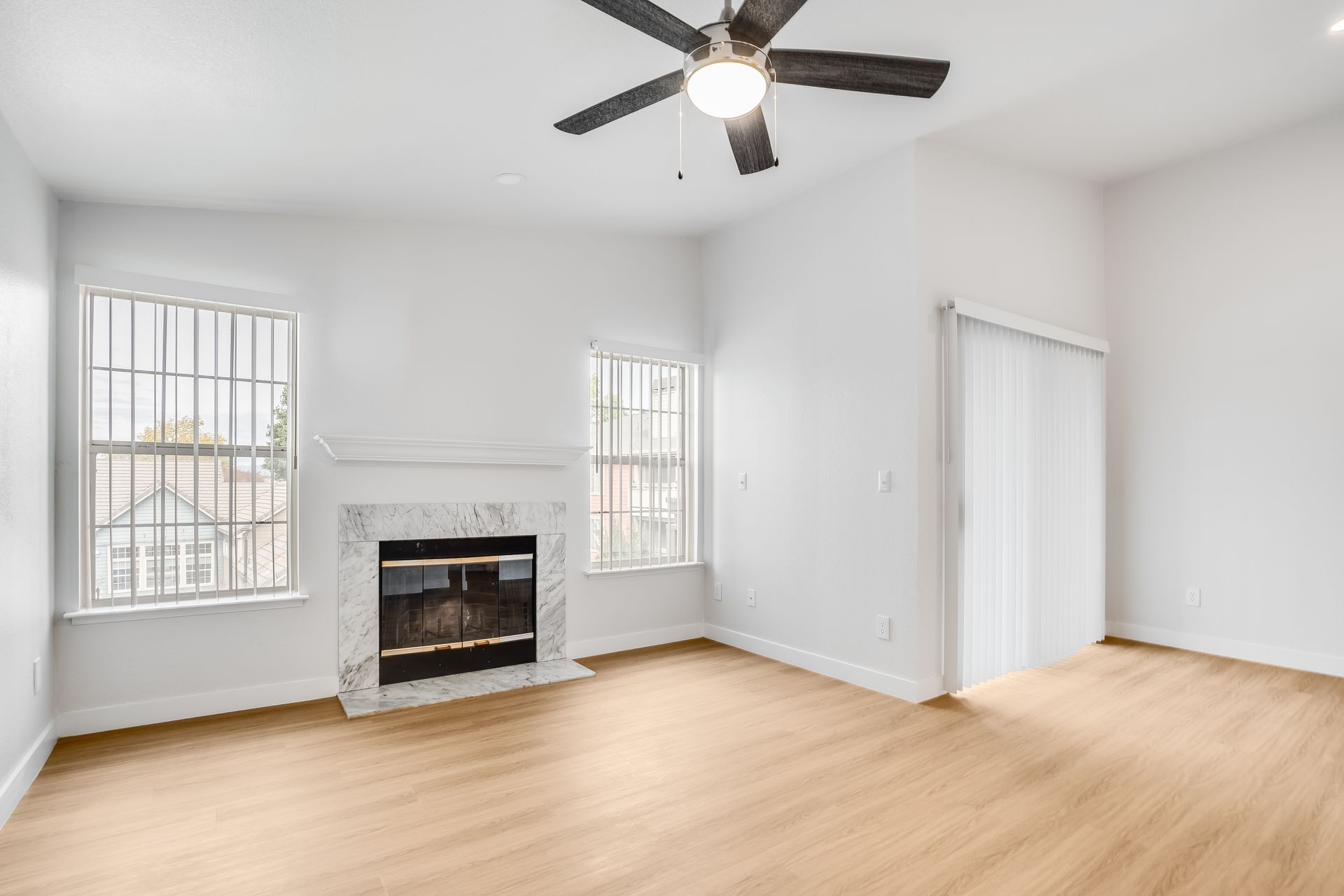 Bright empty bedroom with white walls, wood floors, fireplace, windows, and a ceiling fan
