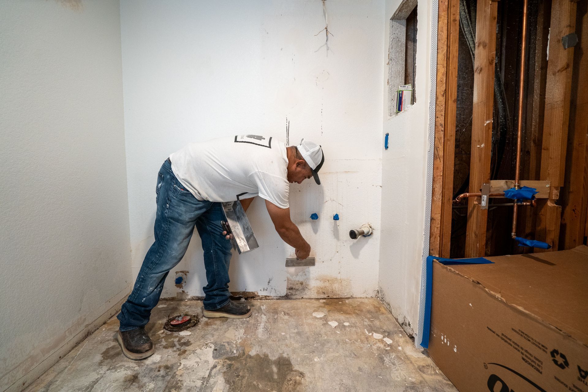 Worker painting a wall corner in a room under renovation, with paint cans and tools nearby