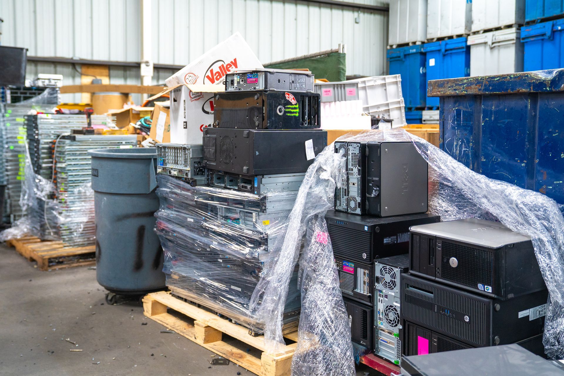Computers and electronics, wrapped in plastic, stacked on pallets in a recycling facility.