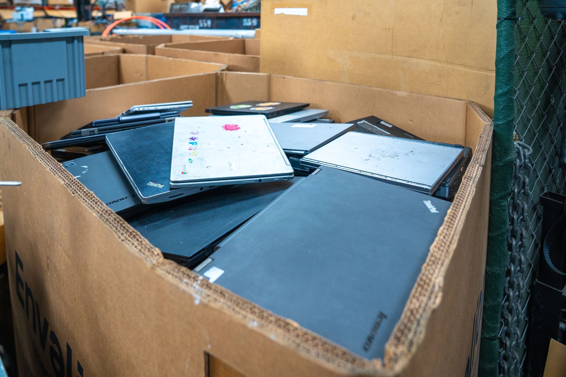 Cardboard bin filled with several closed laptops in a warehouse setting.