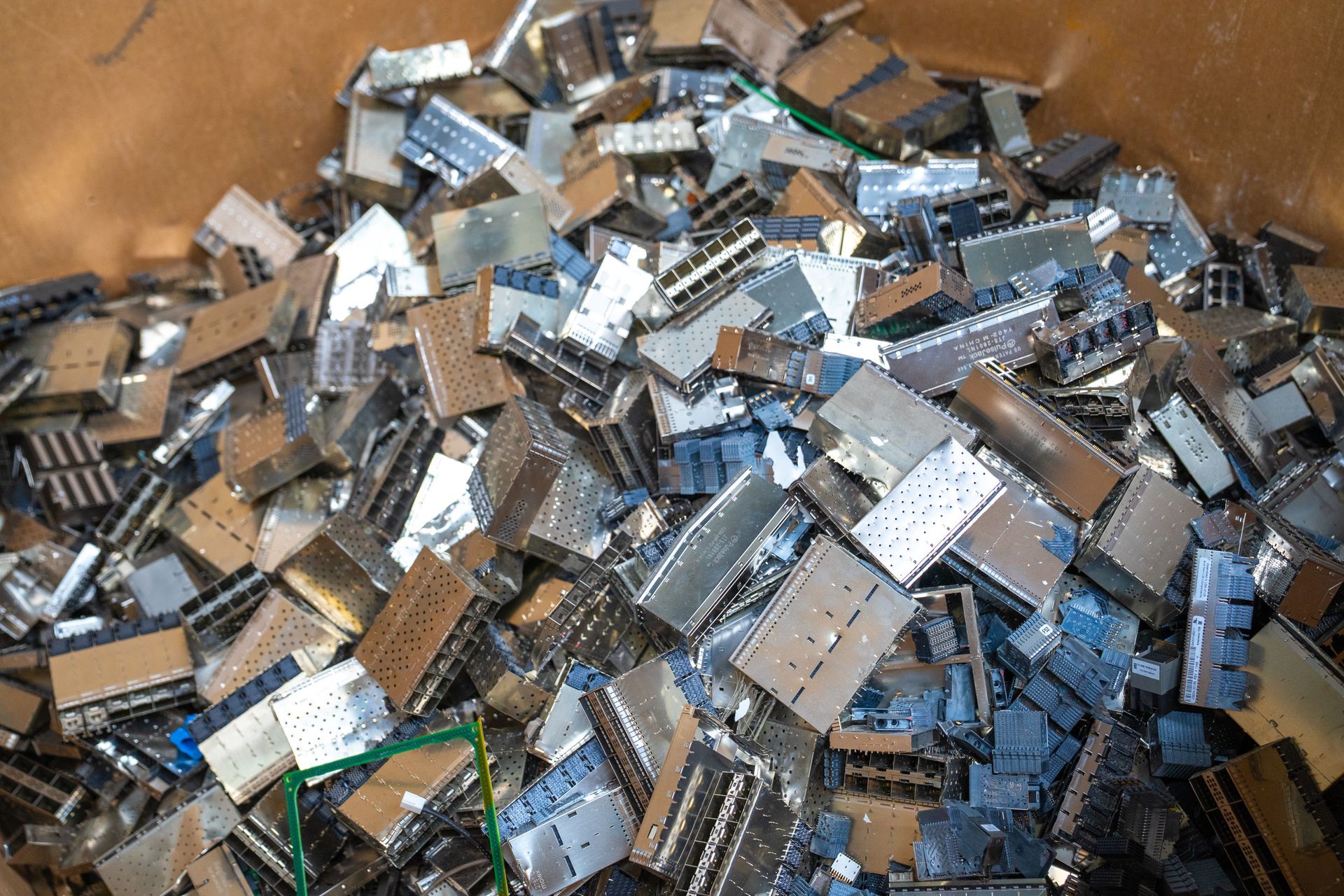 Pile of metallic silver computer components in a brown cardboard box, ready for recycling.