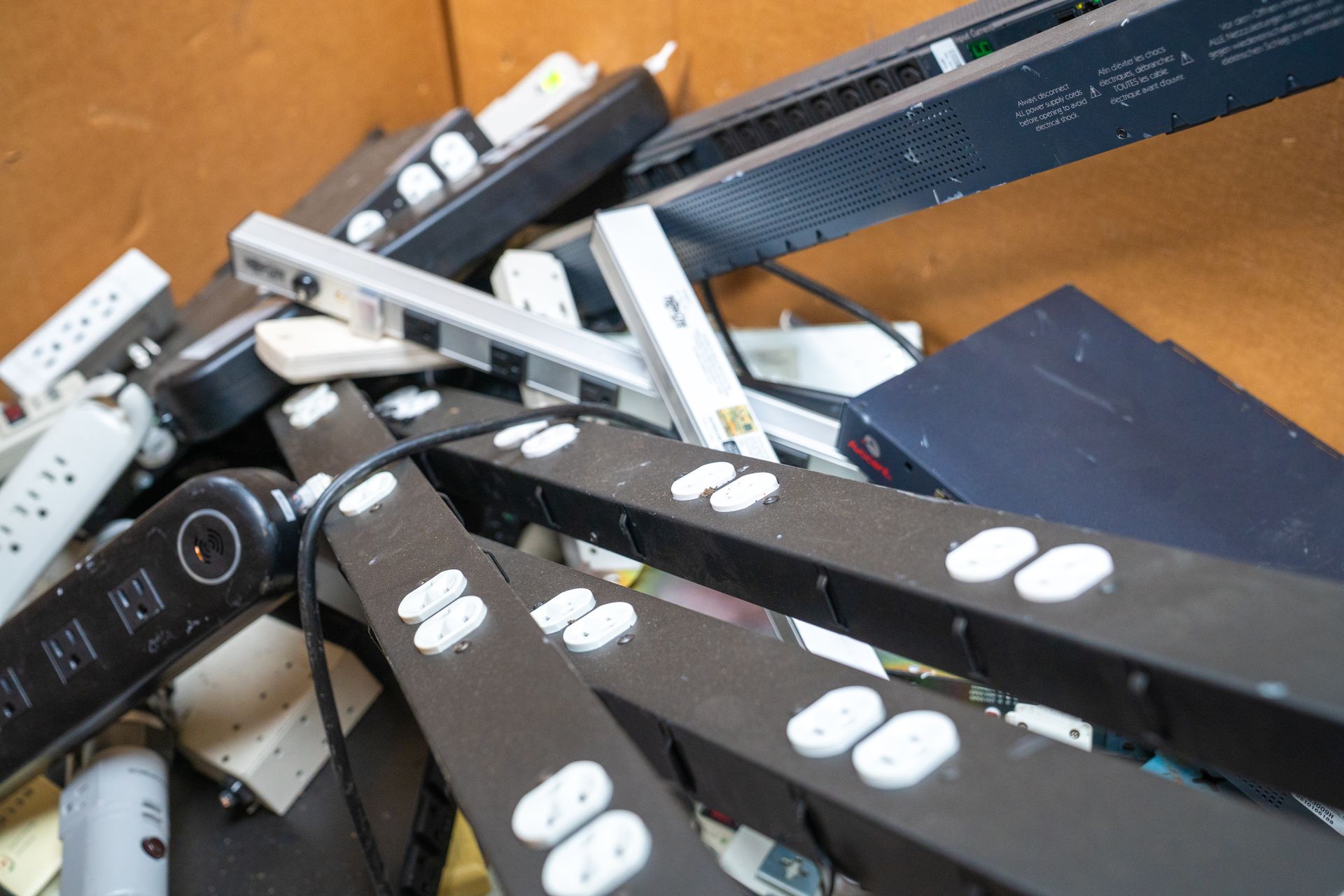A pile of black and white power strips inside a cardboard box.