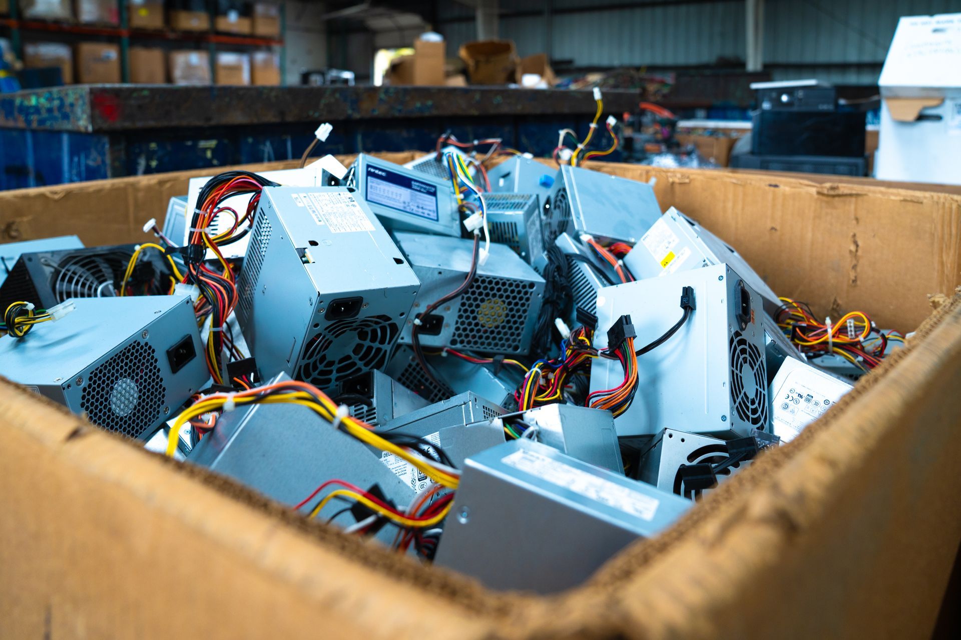 Cardboard box overflowing with computer power supplies, likely for recycling.