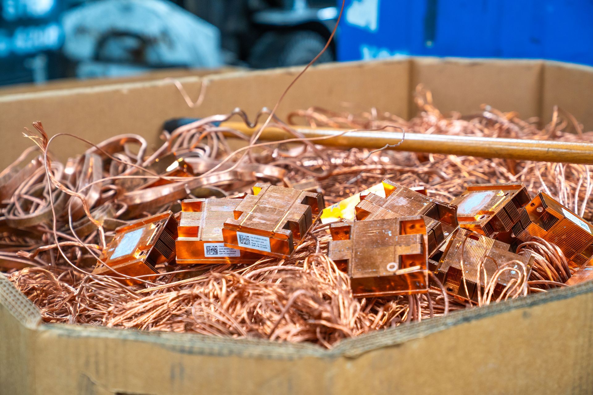 Cardboard box overflowing with copper wires and electronic components at a recycling center.