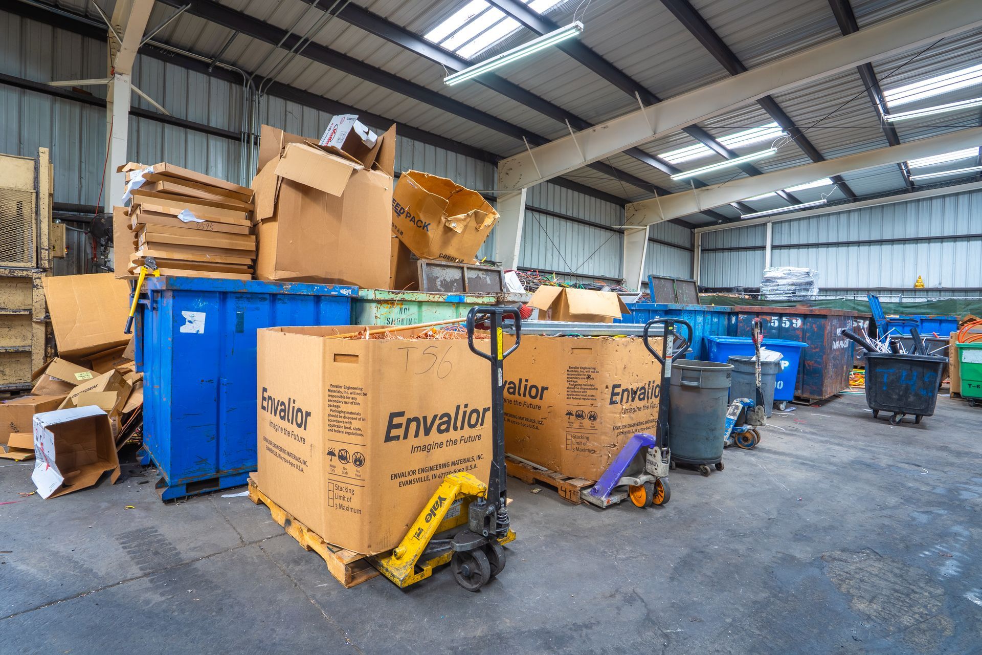 Indoor recycling center with cardboard, bins, and a pallet jack.
