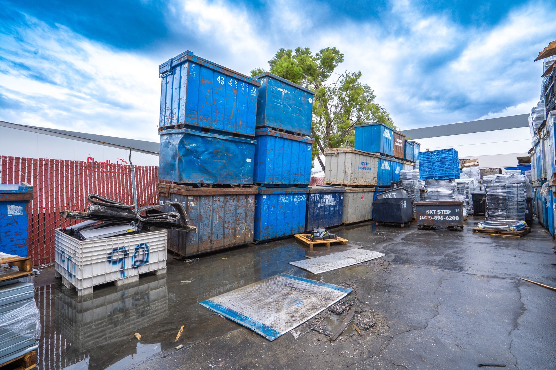 Blue recycling containers stacked outdoors under a cloudy sky.