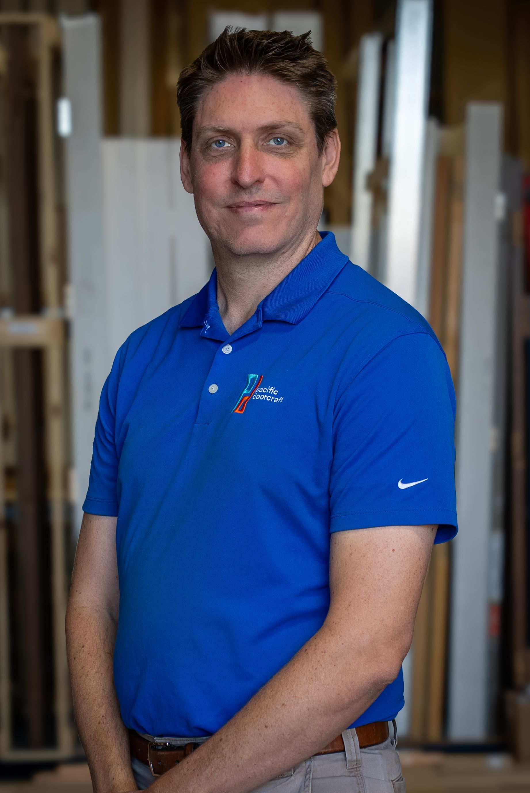 Man in blue polo shirt standing indoors in front of shelves, looking at the camera.