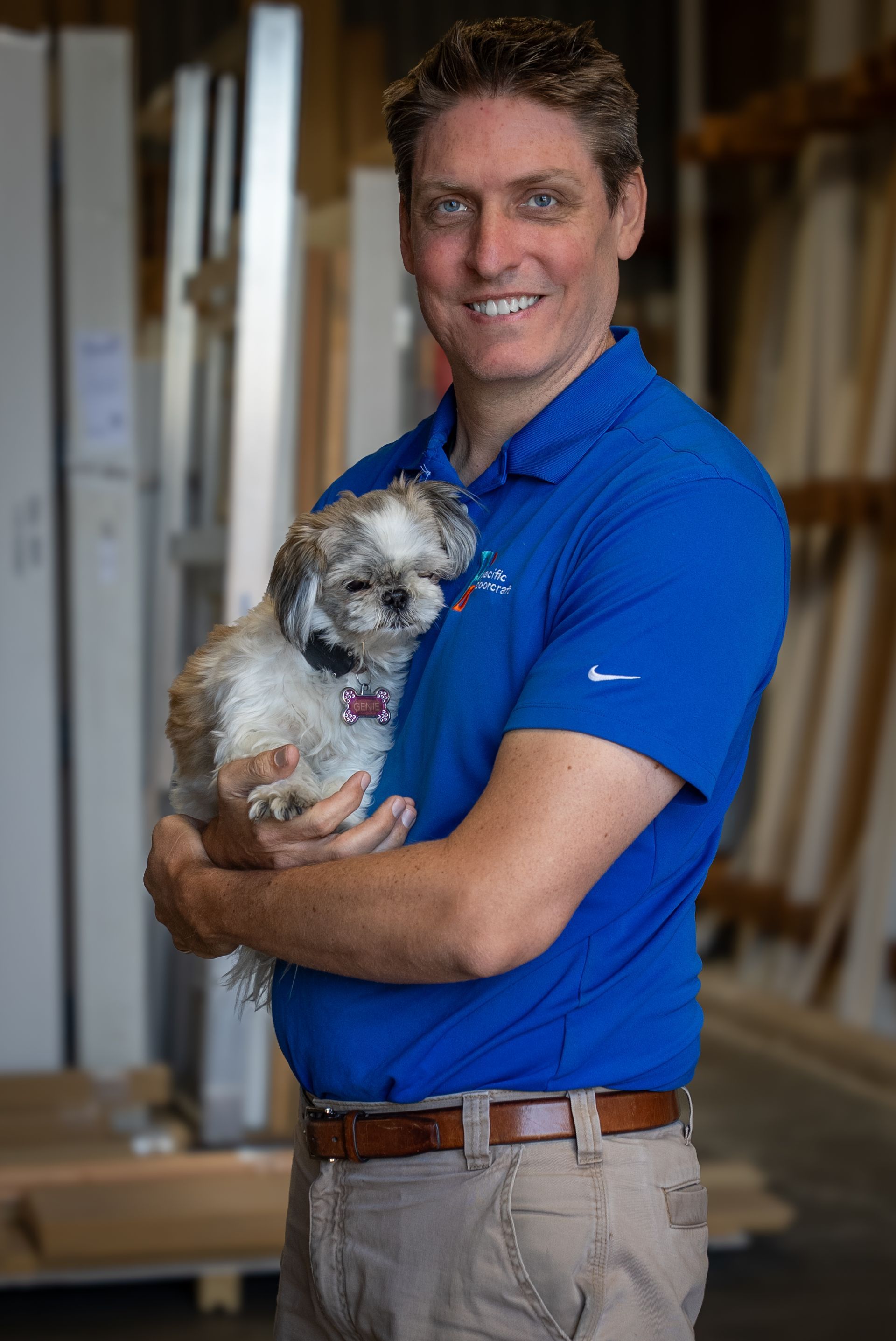 Man in blue polo holding a small gray dog in a workshop setting