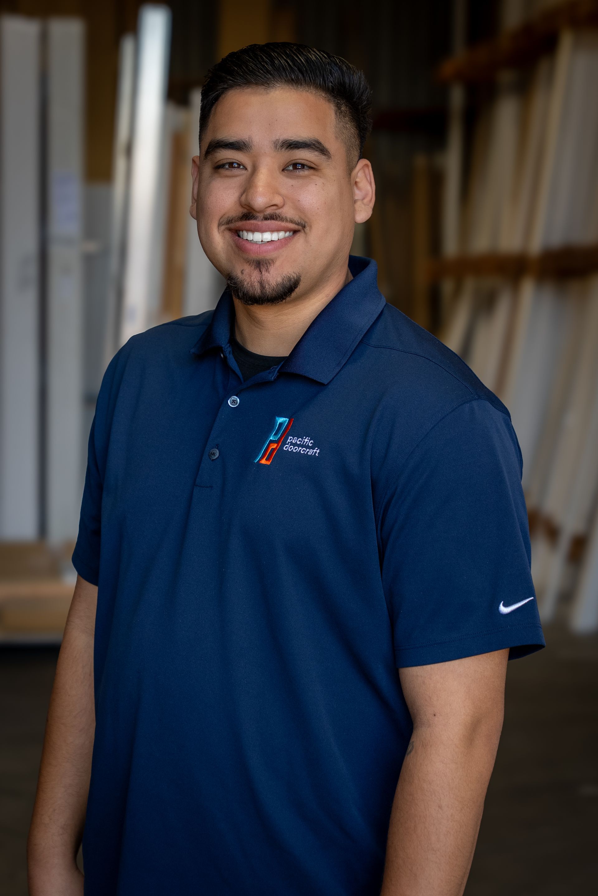 Man smiling in a navy polo shirt, standing indoors with a blurred office or store background
