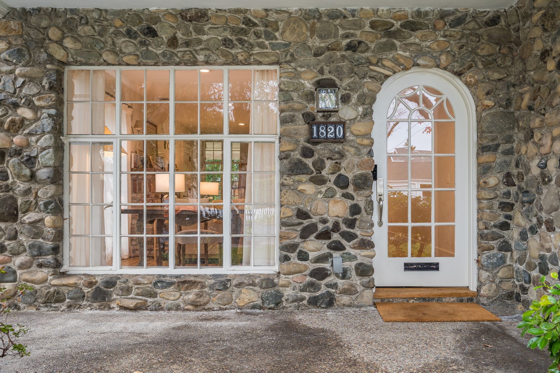Stone house facade with white-framed window, arched door, and number 1680 above the entrance