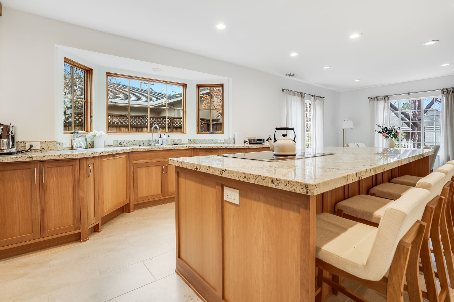 Bright modern kitchen with a large marble island, wood cabinets, and bar stools under recessed lights