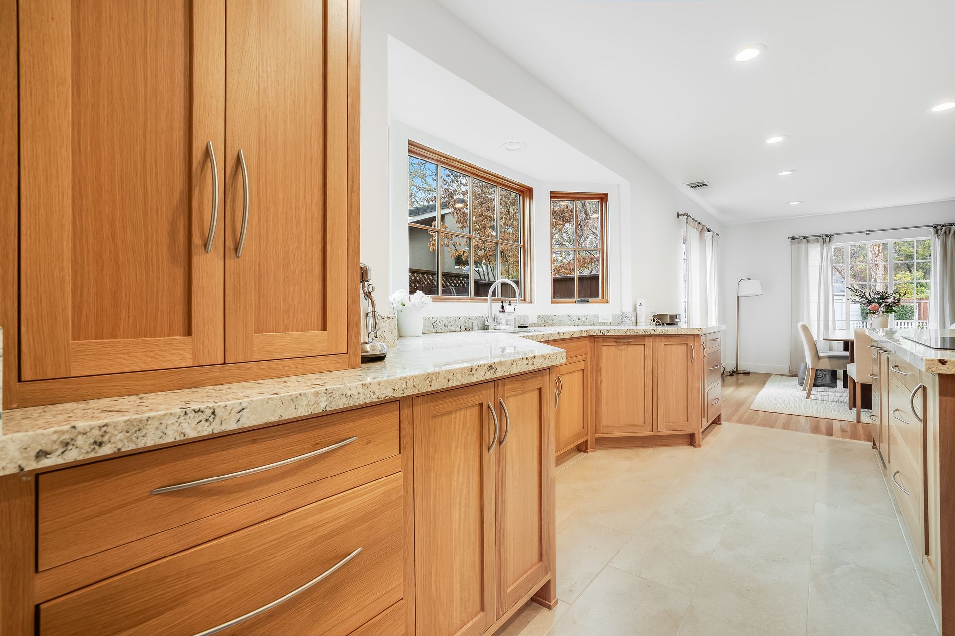 Bright kitchen with wood cabinets, granite counters, and a long view to a dining area and backyard.