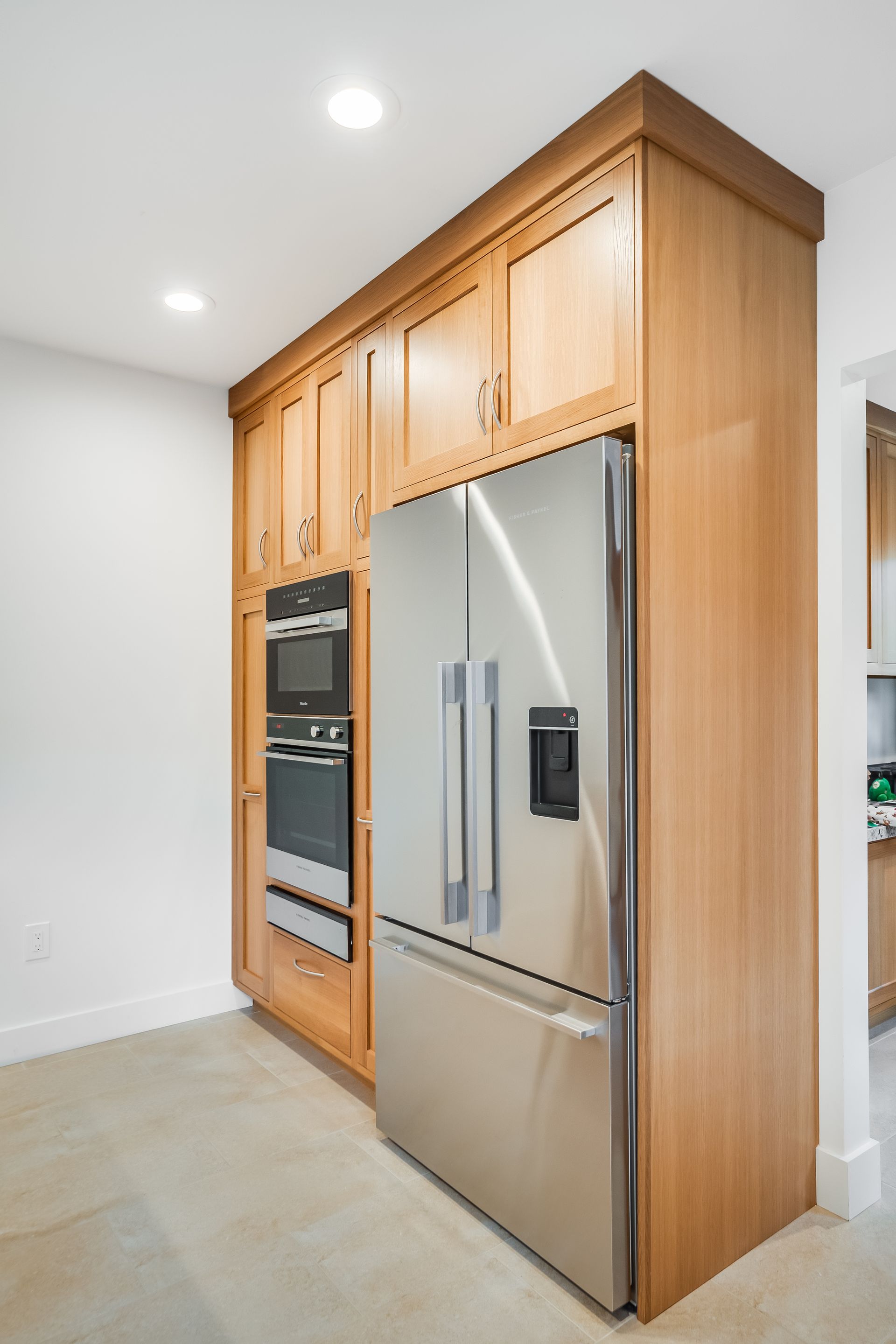Built-in kitchen cabinetry with stainless steel refrigerator and oven, light wood finish