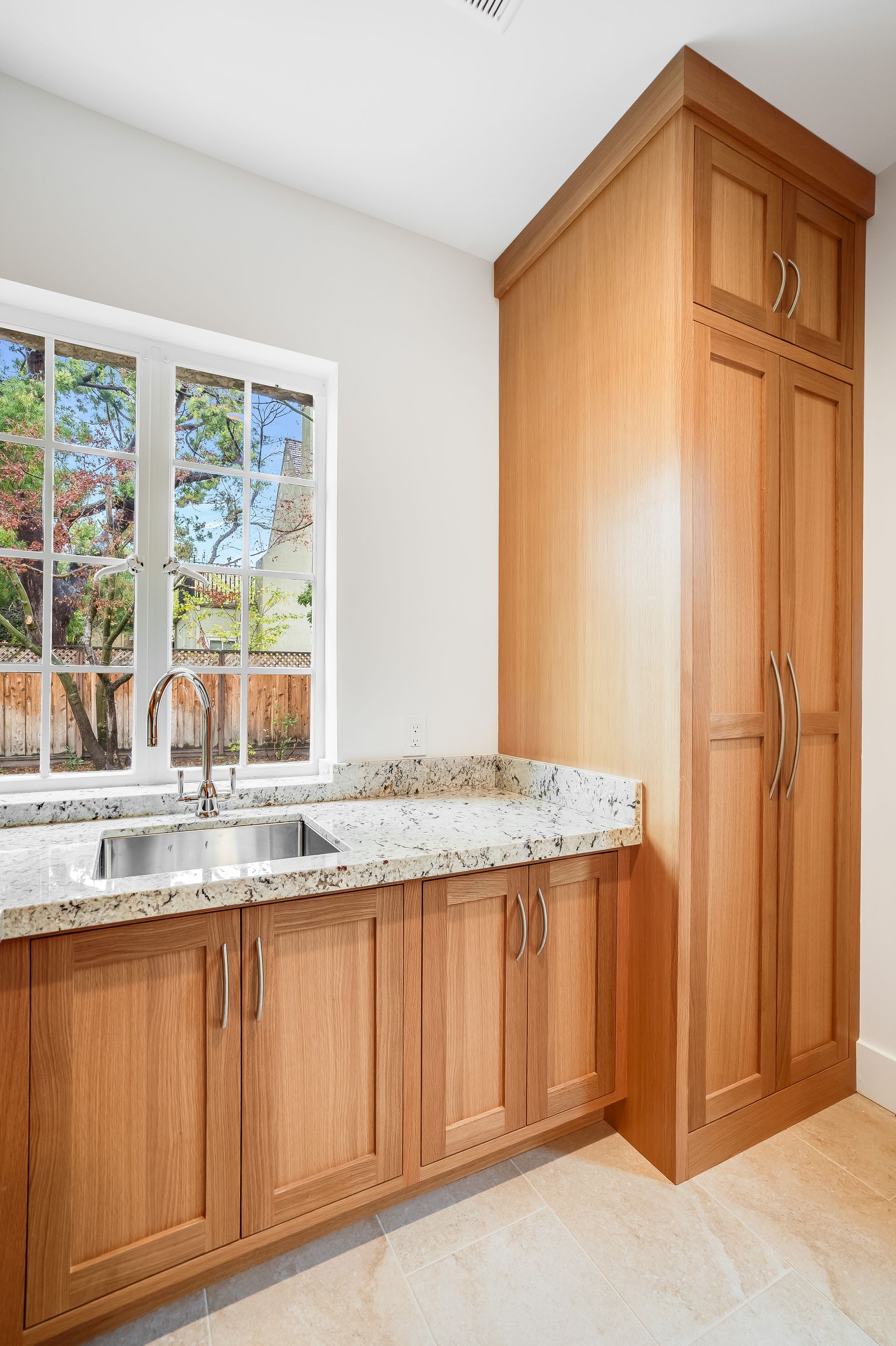 Wooden bathroom vanity with granite countertop and sink under a window, next to a tall storage cabinet.