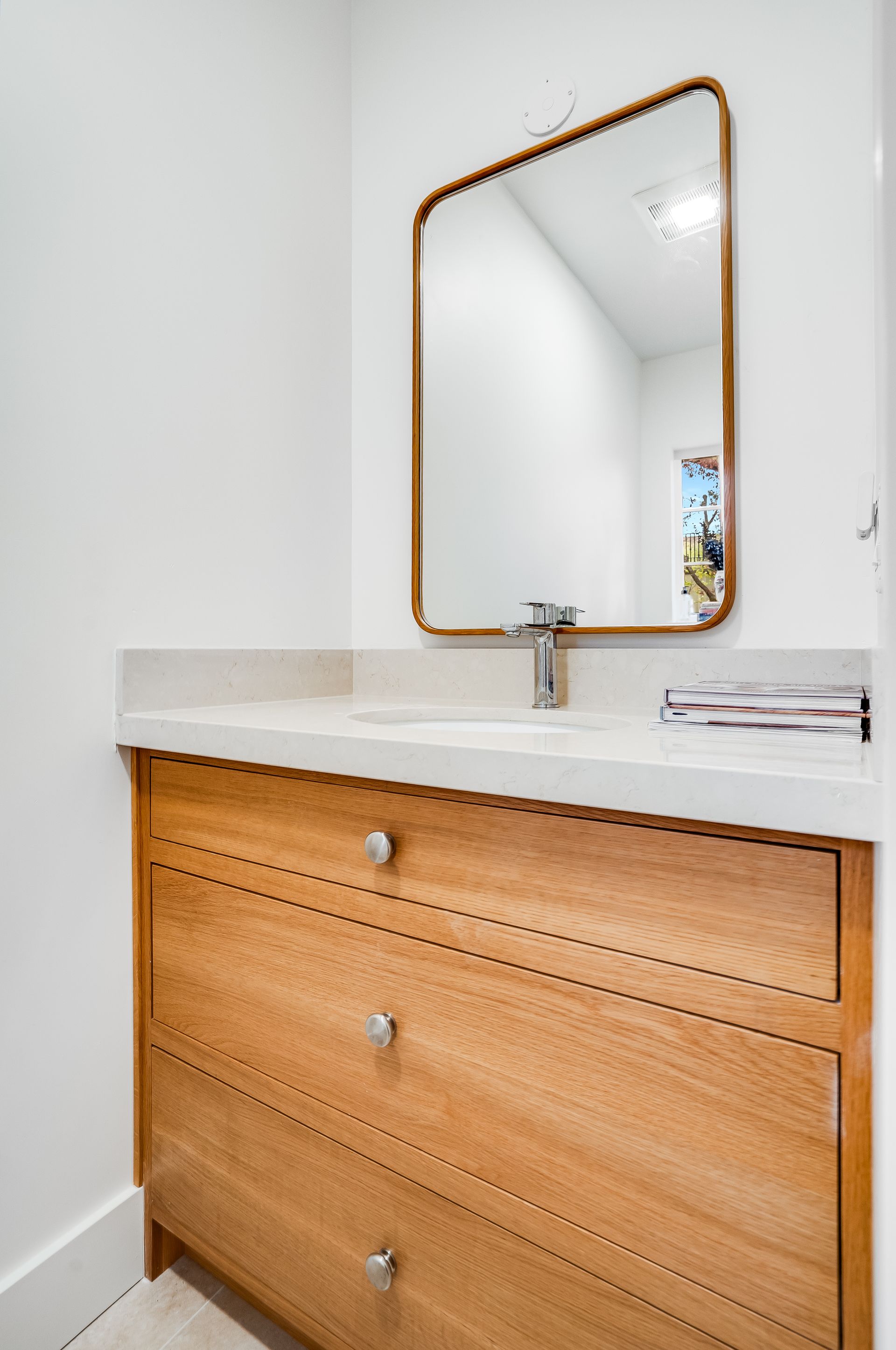 Wooden bathroom vanity with white countertop and gold-framed mirror against a white wall