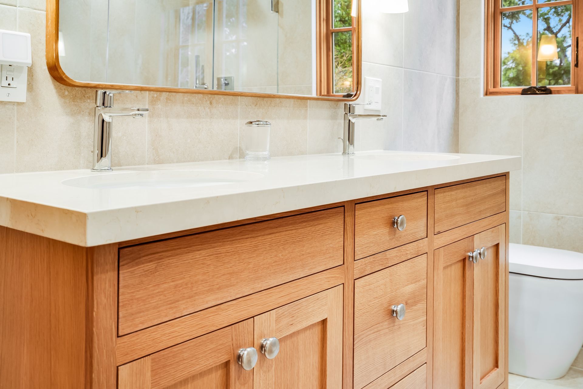 Bathroom vanity with wood cabinets, white countertop, sink, and mirror beside a toilet.
