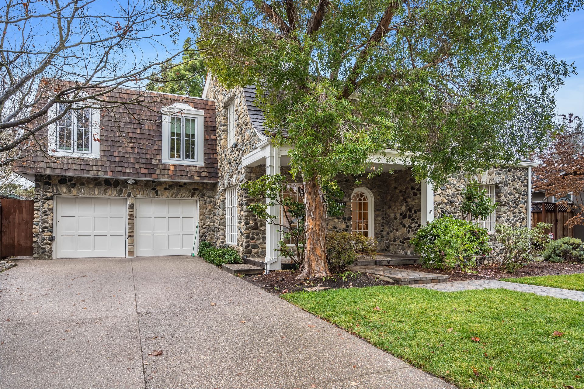 Two-story brick suburban house with double garage, front lawn, and tree-lined driveway