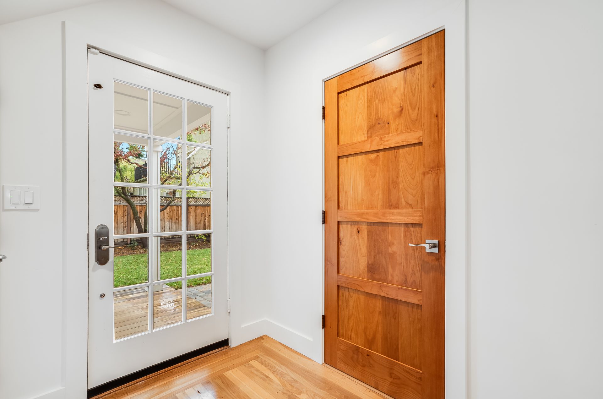 Front entry with a glass-paneled white door and a wooden interior door, bright hardwood floor