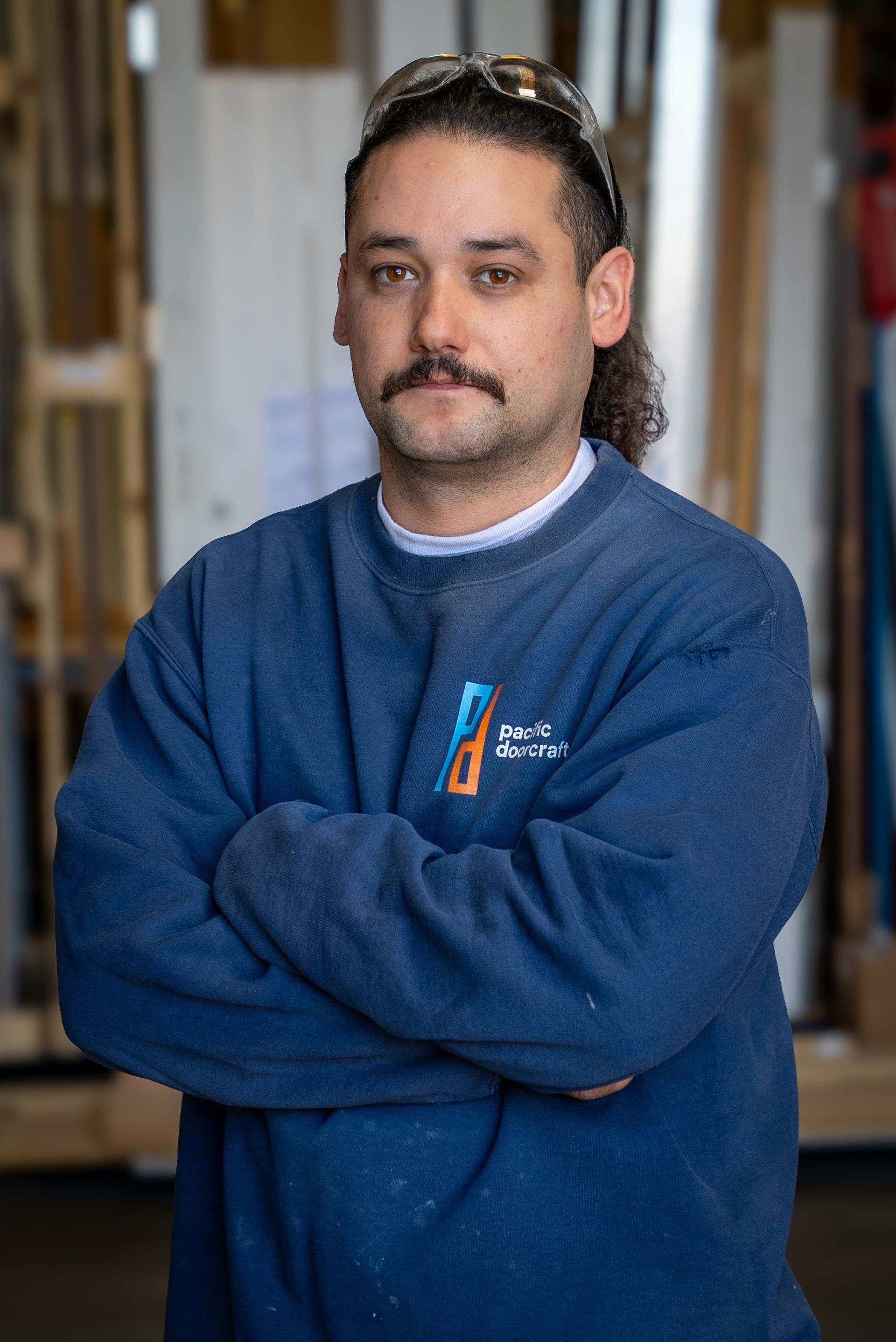 Man standing with arms crossed in a blue sweatshirt in an indoor setting