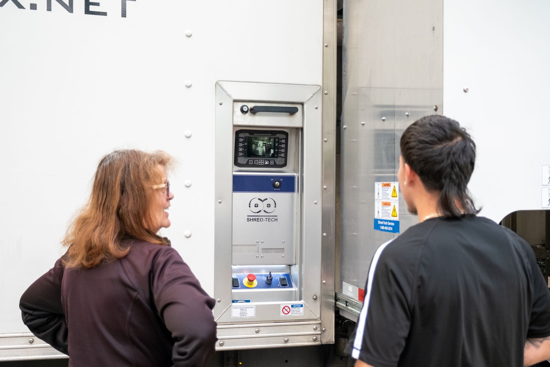 Two people looking at a white truck’s control panel. A small screen displays an image.