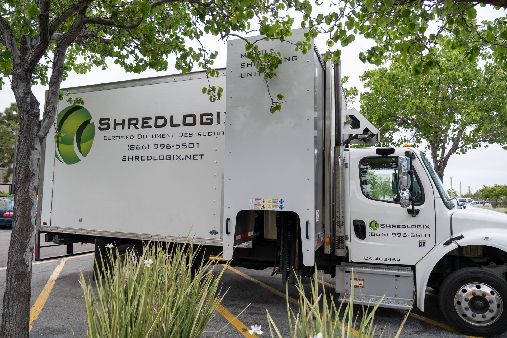 White Shredlogix truck parked under trees.