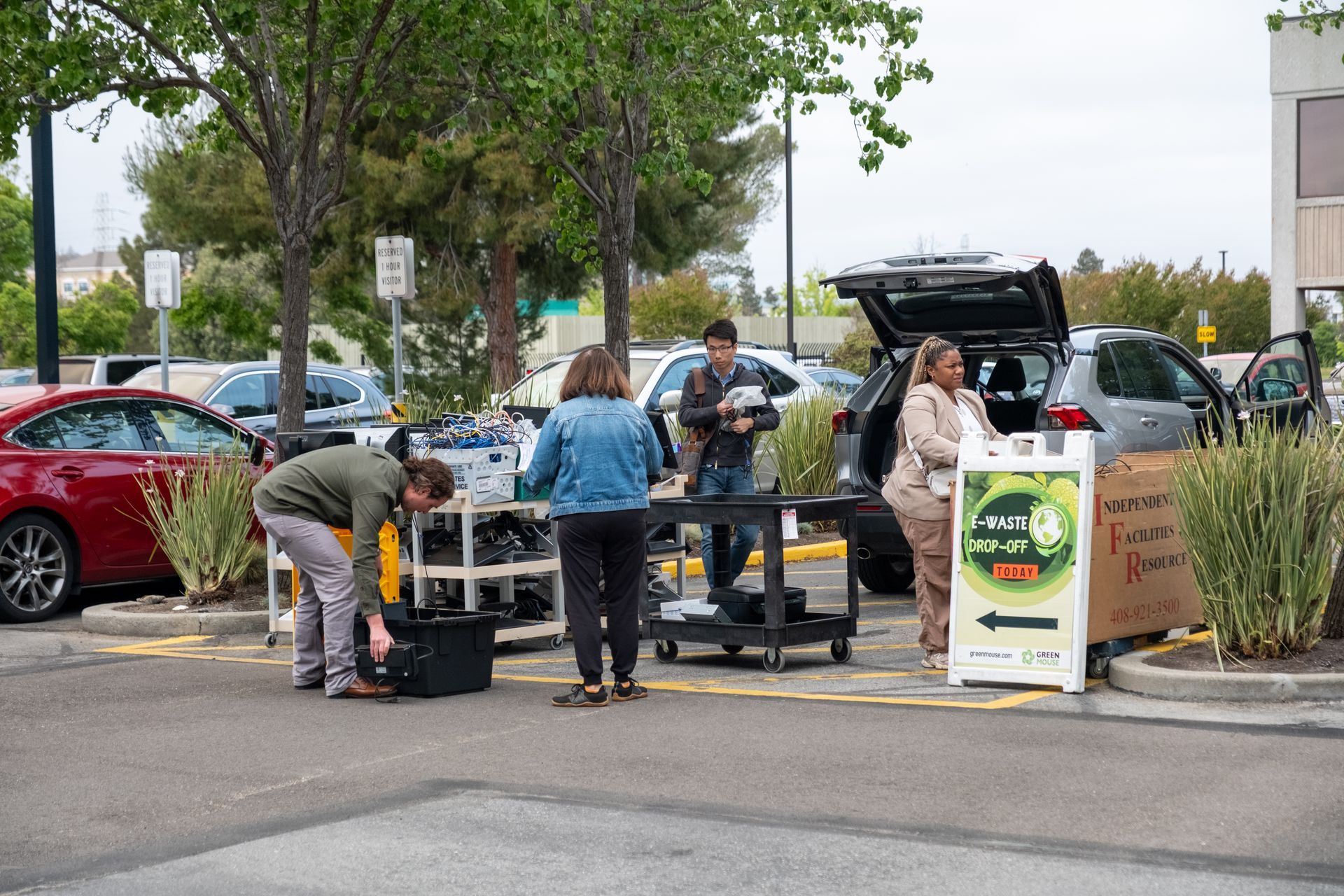People unloading equipment from a car in a parking lot; a sign stands near them.