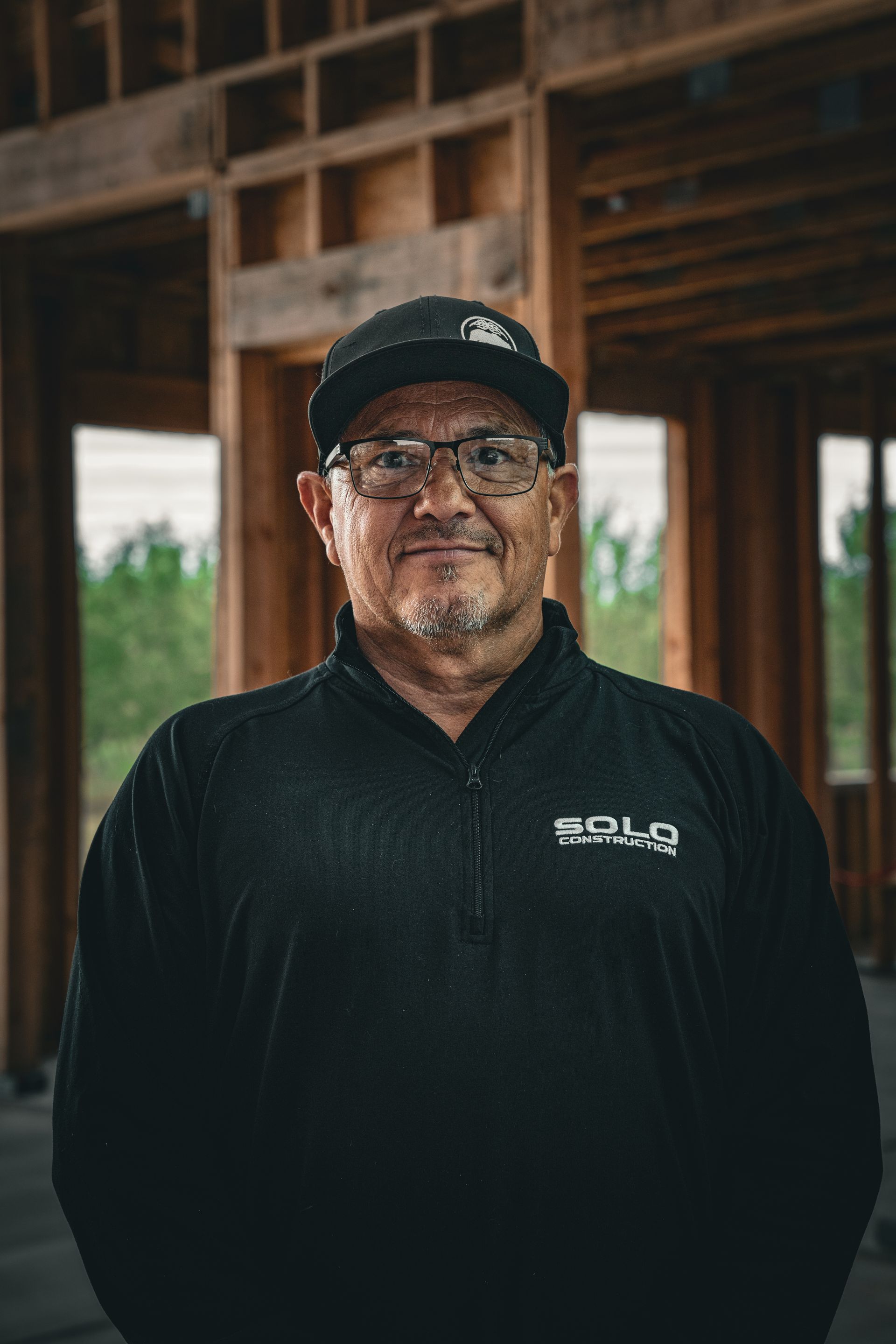 Man in a black cap and jacket standing in a wooden building interior with exposed beams