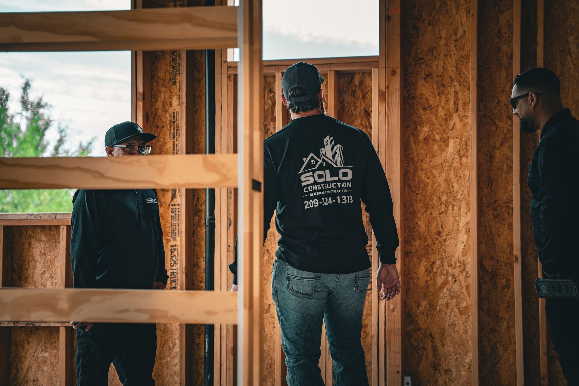 Three people standing inside a wooden-framed house under construction