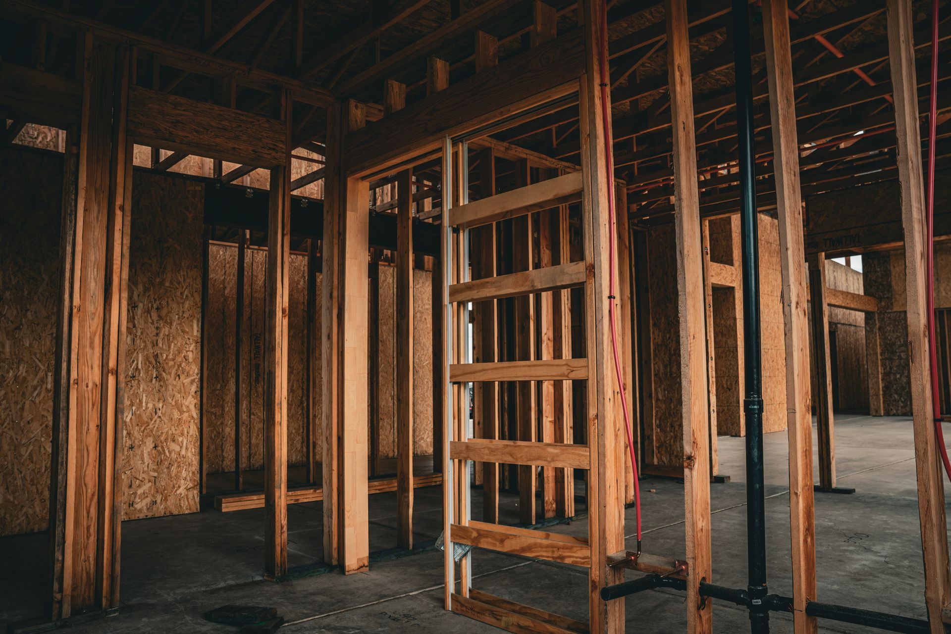 Interior of an unfinished wooden building frame with exposed studs and beams, lit by warm light
